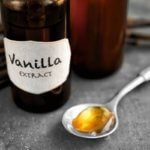 Spoonful of vanilla on table next to bottle of vanilla