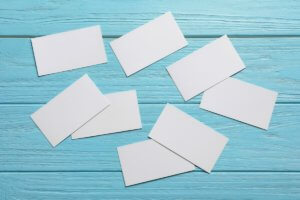 Pile of blank white business cards scattered on a light blue table to introduce topic of producing business cards for your new cookie business