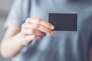 woman in gray t-shirt holding out a blank black business card, to inspire the production of business cards for a new cookie business